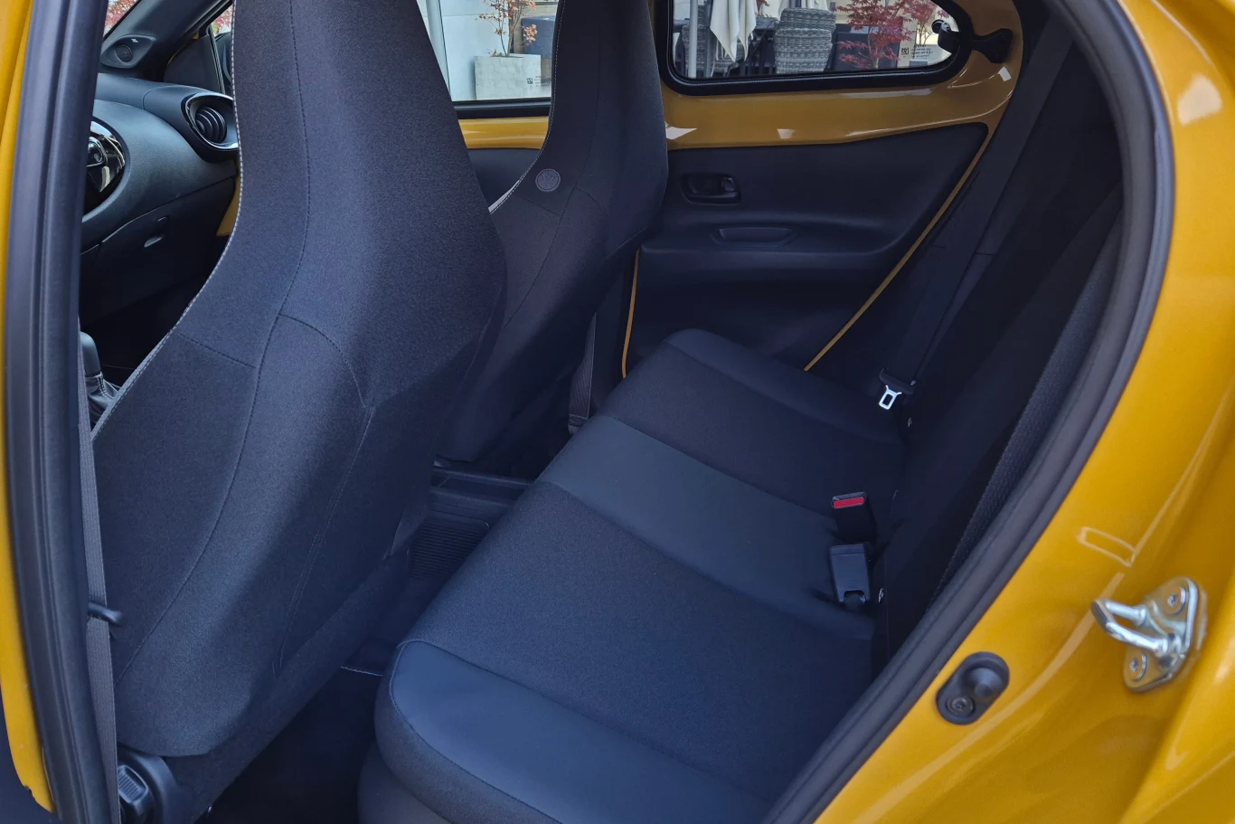 Wnętrze tylnej części samochodu osobowego z czarną tapicerką, żółte drzwi otwarte, widoczna tylna kanapa oraz fragment przednich siedzeń.