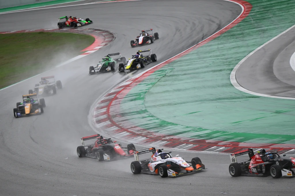 Fot. archiwum: Tymek Kucharczyk Wyścigowe samochody jednomiejscowe rywalizujące na mokrym torze, widoczne rozpryski wody spod kół oraz dynamiczne pokonywanie zakrętu przez kilka pojazdów, otoczenie toru wyścigowego z zielonymi i czerwonymi pasami.