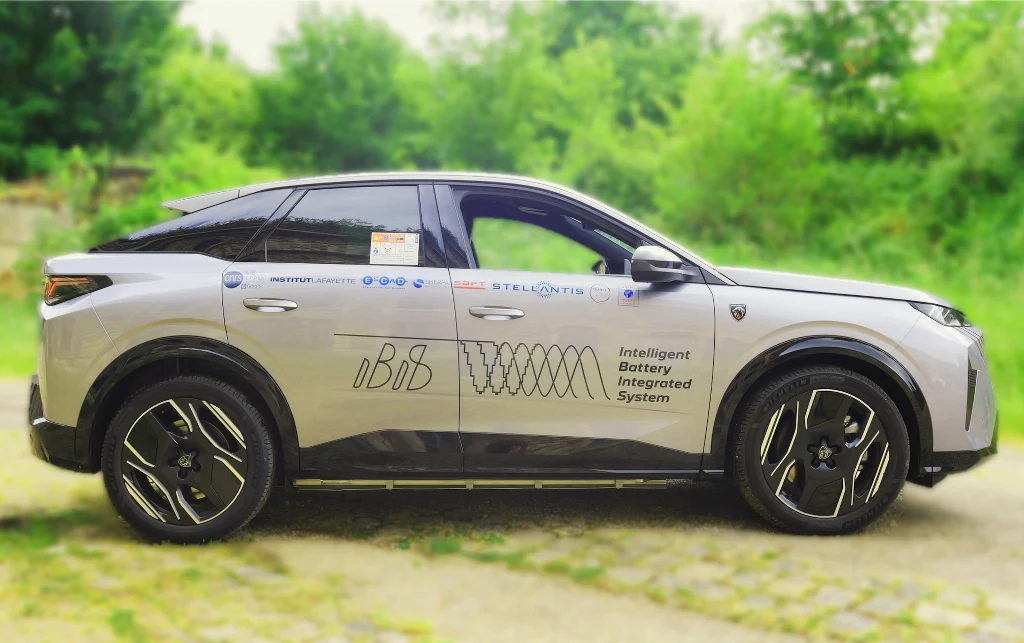 Nowoczesny srebrny samochód elektryczny typu SUV z oznaczeniami producenta oraz napisem Intelligent Battery Integrated System na bocznych drzwiach, ustawiony na tle zieleni i rozmytego naturalnego otoczenia.