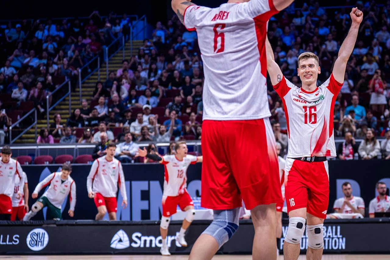 Polscy siatkarze w biało-czerwonych strojach świętują zdobycie punktu lub zwycięstwo, unosząc ramiona w geście tryumfu, na tle pełnej widowni i sportowej hali.