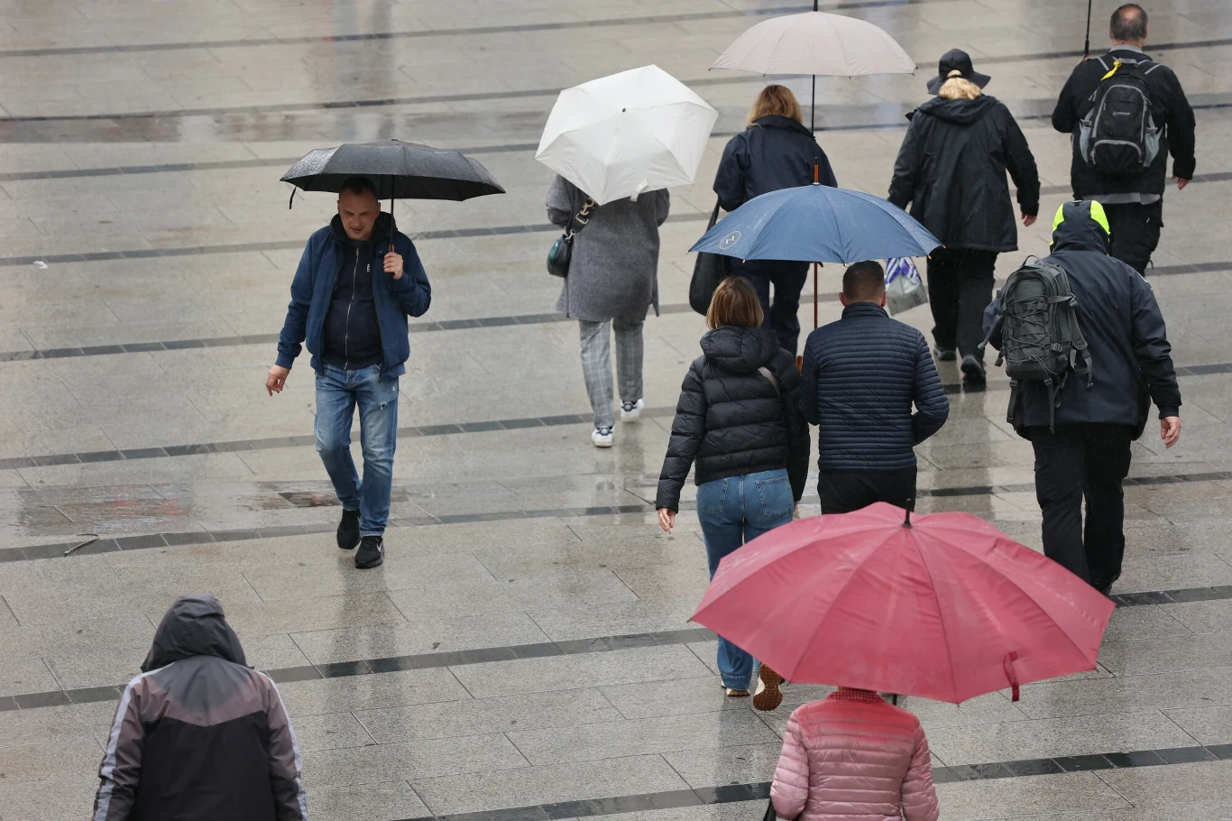 Liczba ludności Polski na koniec lipca spadła poniżej poziomu 37,4 mln - wynika z tabel GUS Ludzie idący po mokrym chodniku w deszczowy dzień, trzymający kolorowe parasole, większość z nich ubrana w kurtki i płaszcze chroniące przed pogodą.