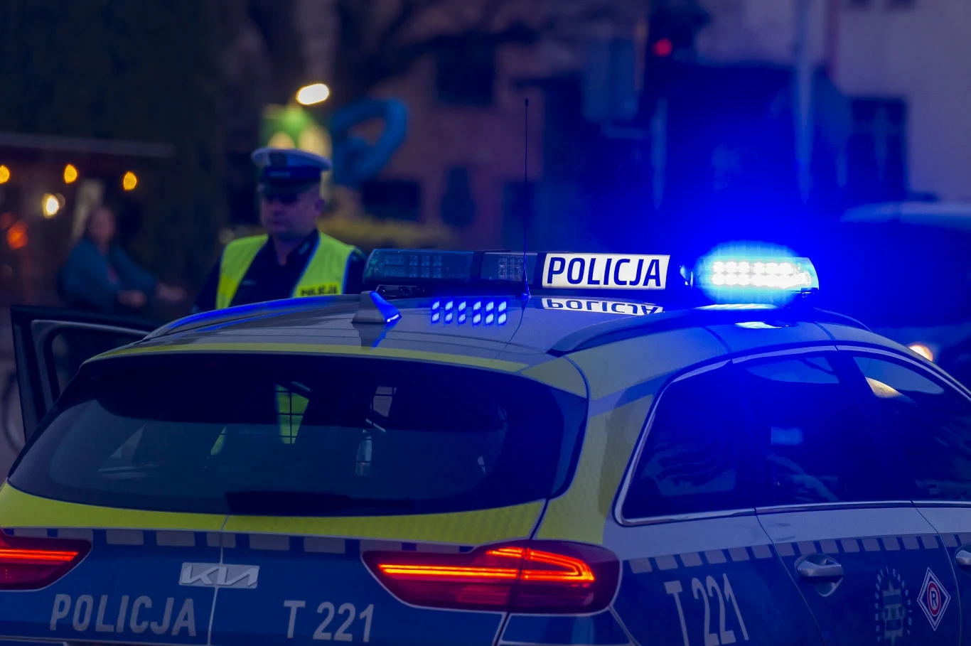 Szczecin kontra głośne auta i motocykle. Jest petycja mieszkańców Radiowóz policyjny z włączonymi niebieskimi światłami na dachu, stojący na ulicy, obok funkcjonariusz policji w żółtej kamizelce odblaskowej.