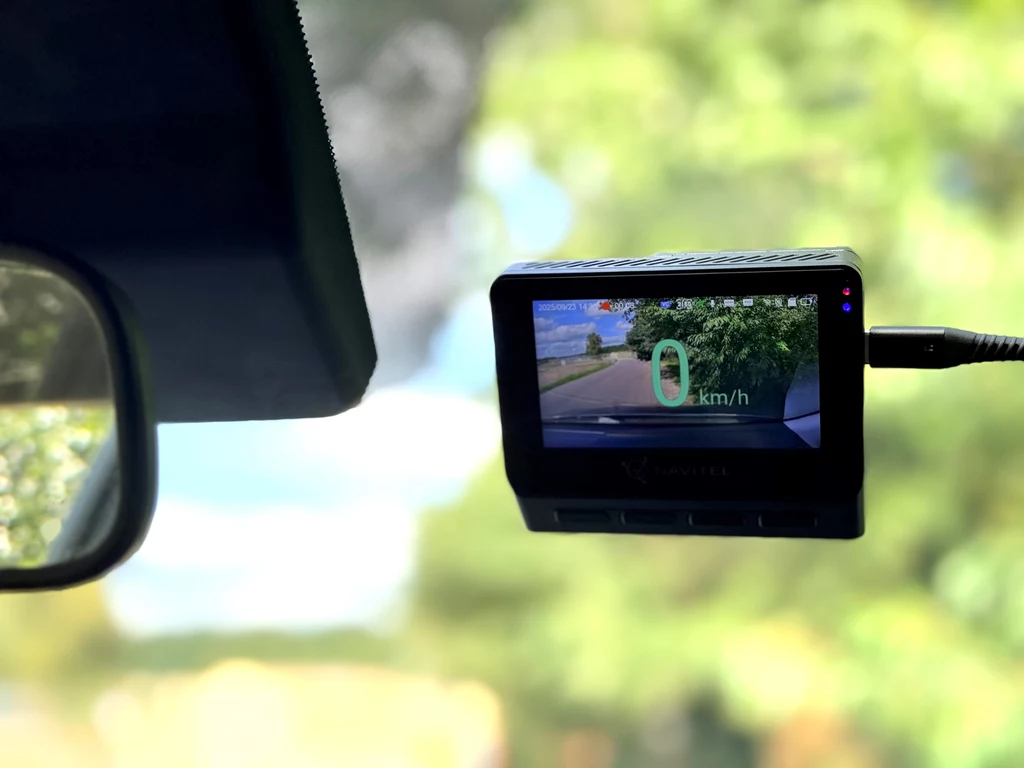 Kamera samochodowa zamontowana na przedniej szybie pojazdu rejestruje drogę oraz wyświetla informację o aktualnej prędkości 0 km/h na cyfrowym ekranie.