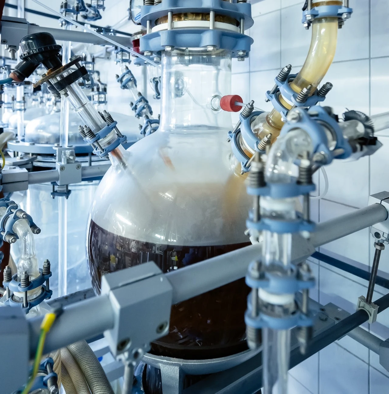 Biophelion chce w przyszłości pozyskiwać nowe materiały nadające się do recyklingu z odpadów przemysłowych. Duża szklana kolba laboratoryjna wypełniona ciemną cieczą, otoczona rozbudowaną instalacją z rurkami i zaworami, wszystko utrzymane w sterylnych, przemysłowych warunkach.