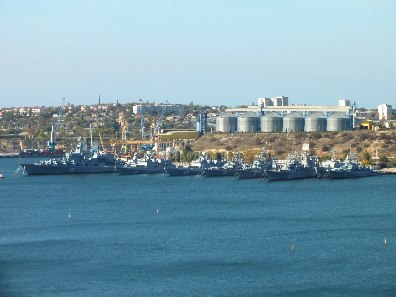 Dziennikarskie śledztwo w sprawie chińskiego statku, który pojawiał się na Krymie (zdjęcie ilustracyjne) Okręty wojenne zacumowane przy nabrzeżu w porcie, w tle widoczne magazyny przemysłowe oraz niewielka część zabudowy miejskiej.