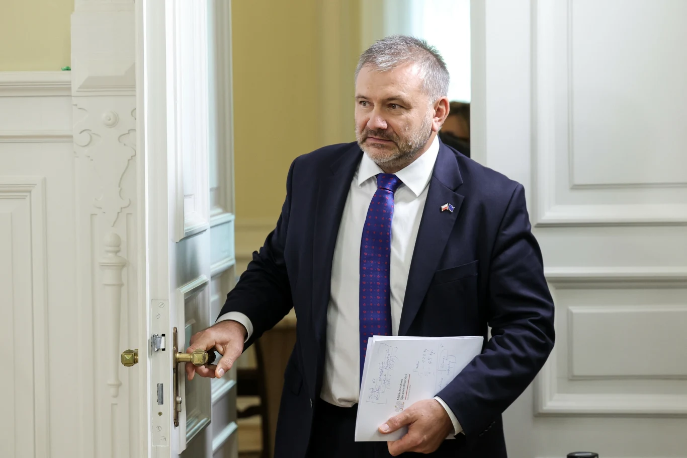 Minister sprawiedliwości i prokurator generalny Waldemar Żurek Mężczyzna w garniturze z teczką dokumentów w ręku przekracza próg drzwi biurowych, wygląda na skupionego i eleganckiego, wnętrze pomieszczenia jest jasne i formalne