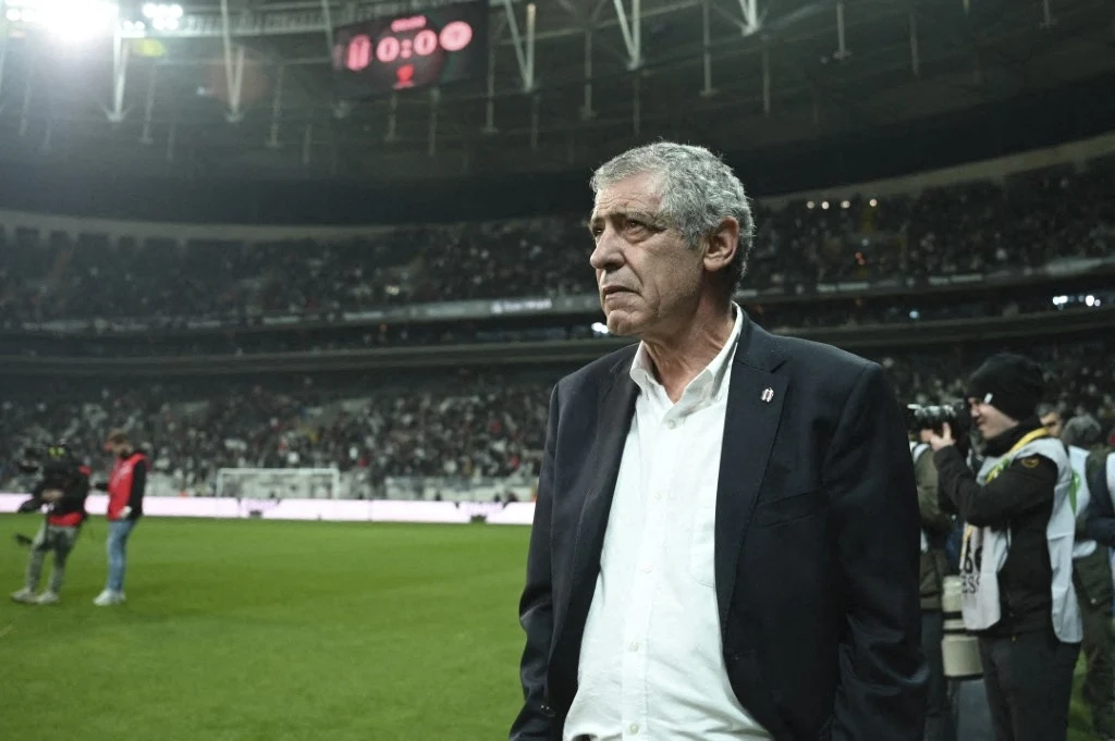 Były trener polskich piłkarzy Fernando Santos zainwestował w zabawki edukacyjne Starszy mężczyzna w garniturze stoi na murawie stadionu, w tle trybuny wypełnione kibicami oraz ludzie wykonujący zdjęcia.