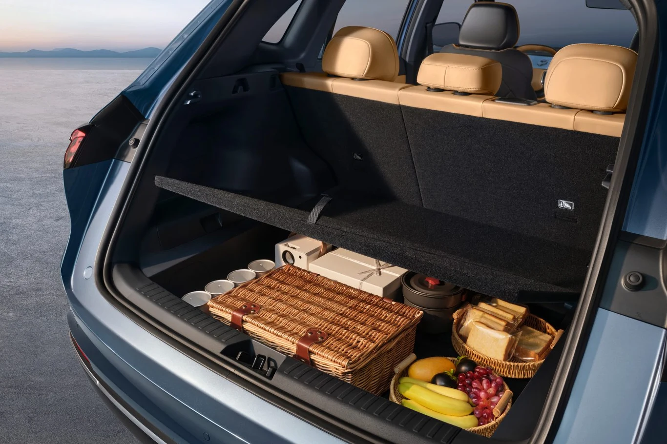 Otwarte bagażnik samochodu terenowego, w środku znajduje się wiklinowy kosz piknikowy, na półce ułożone są talerze, świeże owoce, pieczywo oraz zestaw kubków do napojów. Składane siedzenia tylne zapewniają dodatkową przestrzeń na większy ładunek. Wnętr...