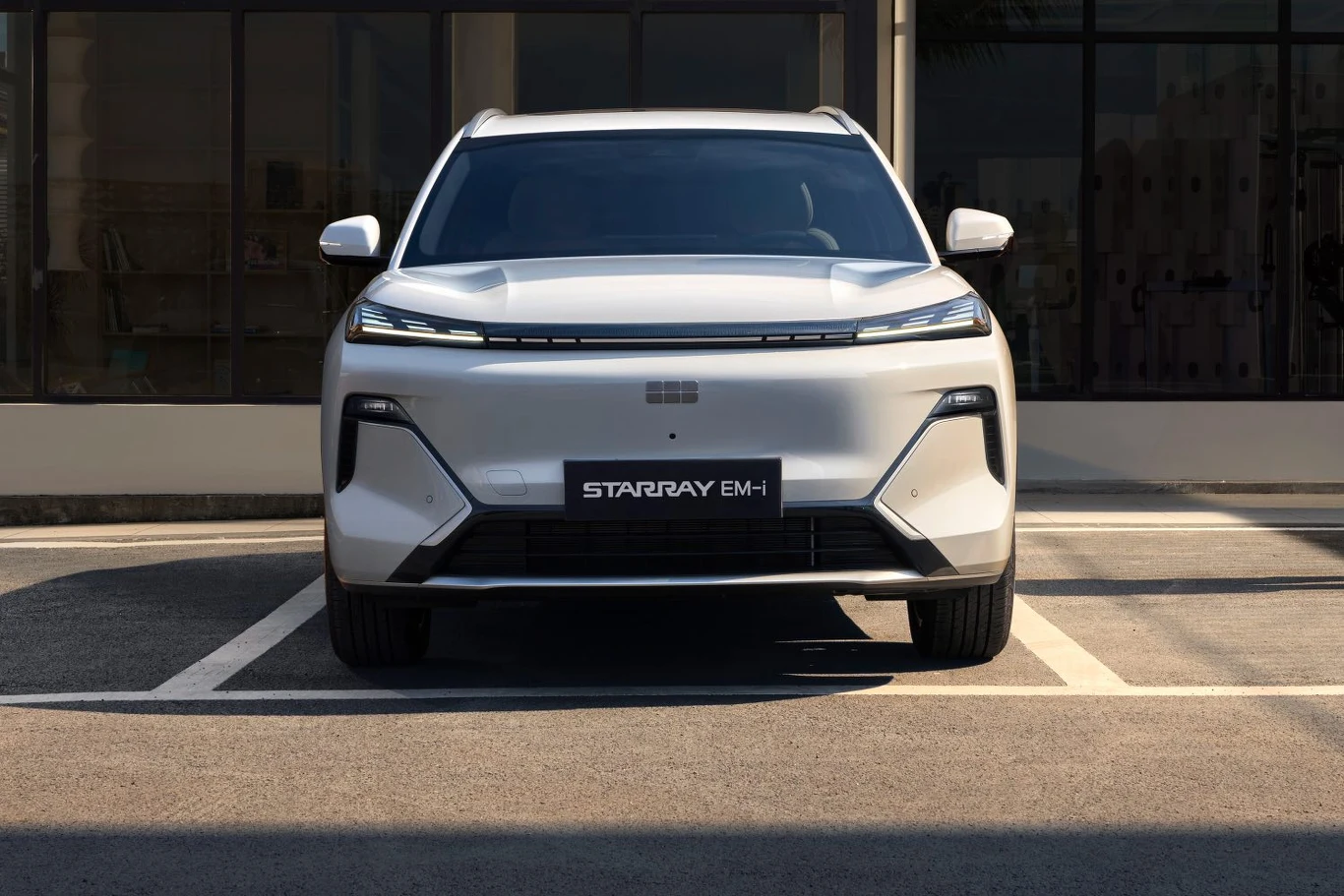 Nowoczesny biały samochód SUV marki StarRay BM-1 zaparkowany na wyznaczonym miejscu parkingowym przed budynkiem z dużymi oknami.