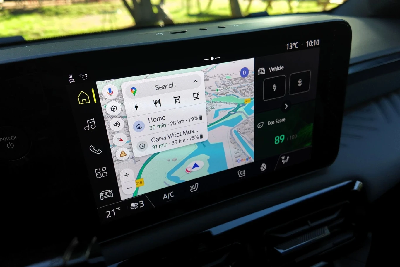 System multimediów Nissana Micry bazuje na Android Automotive. Oznacza to, że mamy dostęp do wbudowanych usług Google. Wnętrze samochodu z dużym ekranem systemu multimedialnego wyświetlającym mapę nawigacji, trasę do domu oraz inne punkty docelowe, widoczne ikony ustawień klimatyzacji i podgląd statusu pojazdu.