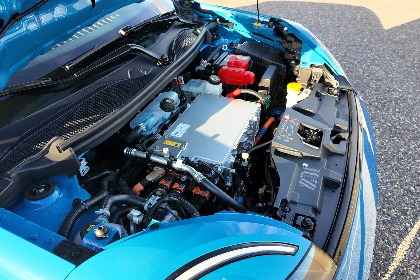 Nissan Micra dostępny jest w dwóch wariantach napędu - 120 KM i 150 KM. Otwarta maska niebieskiego samochodu ukazująca nowoczesny silnik elektryczny z widocznymi przewodami, sterownikami i innymi podzespołami mechaniczno-elektronicznymi.