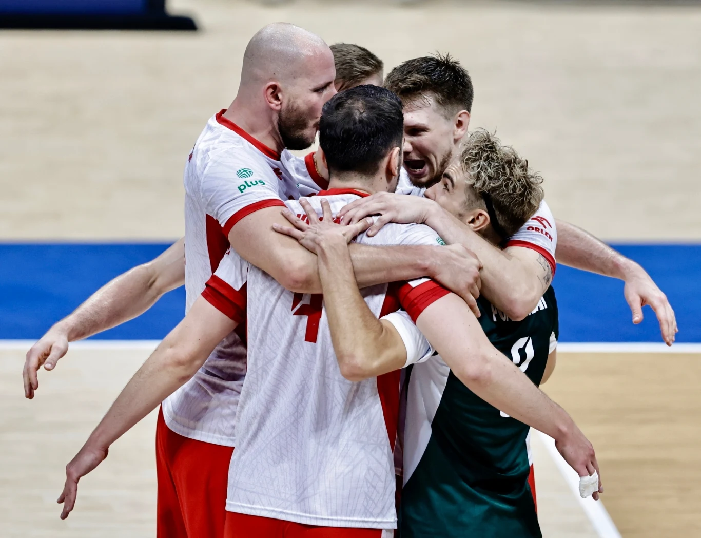 Grupa siatkarzy w sportowych strojach obejmuje się na środku boiska, wyrażając radość po zdobyciu punktu podczas meczu.