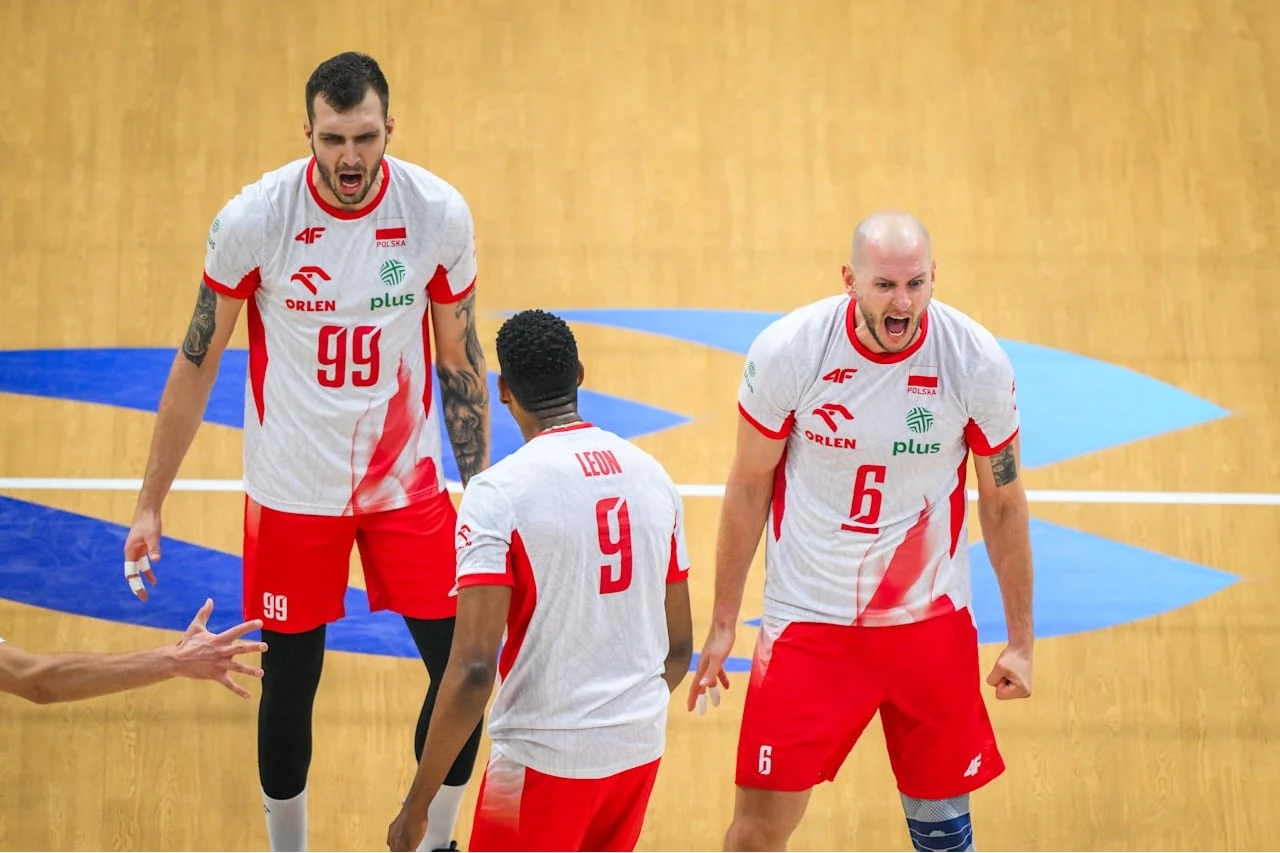 Trzech siatkarzy reprezentacji Polski w białych koszulkach z czerwonymi spodenkami świętuje zdobycie punktu na boisku, widoczne emocje i entuzjazm zawodników.