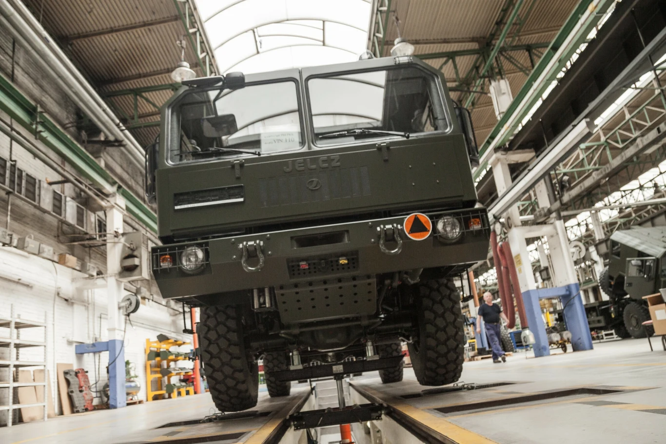 Śląsk przed transformacją. Zagłębie węgla stanie się hubem obronnym Polski? Wojskowy pojazd ciężarowy marki Jelcz ustawiony na stanowisku serwisowym w dużej, jasnej hali fabrycznej, w otoczeniu elementów technicznych i osób pracujących w tle.