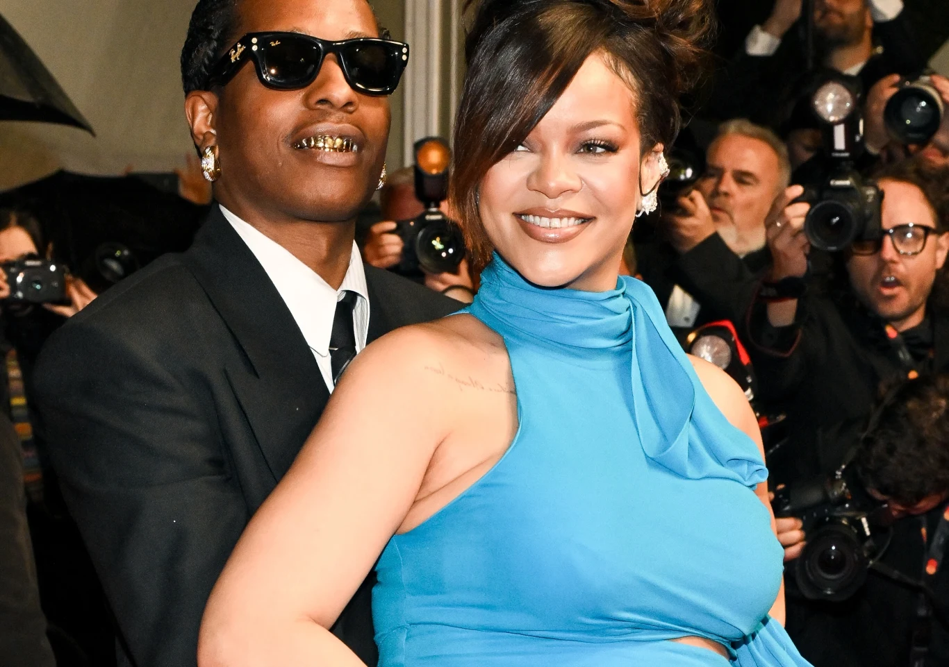 A$AP Rocky i Rihanna powitali na świecie pierwszą córeczkę Para uśmiechających się osób ubranych elegancko, jedna z nich ma na sobie garnitur i okulary przeciwsłoneczne, druga suknię w kolorze błękitnym, w tle wielu fotografów z aparatami.
