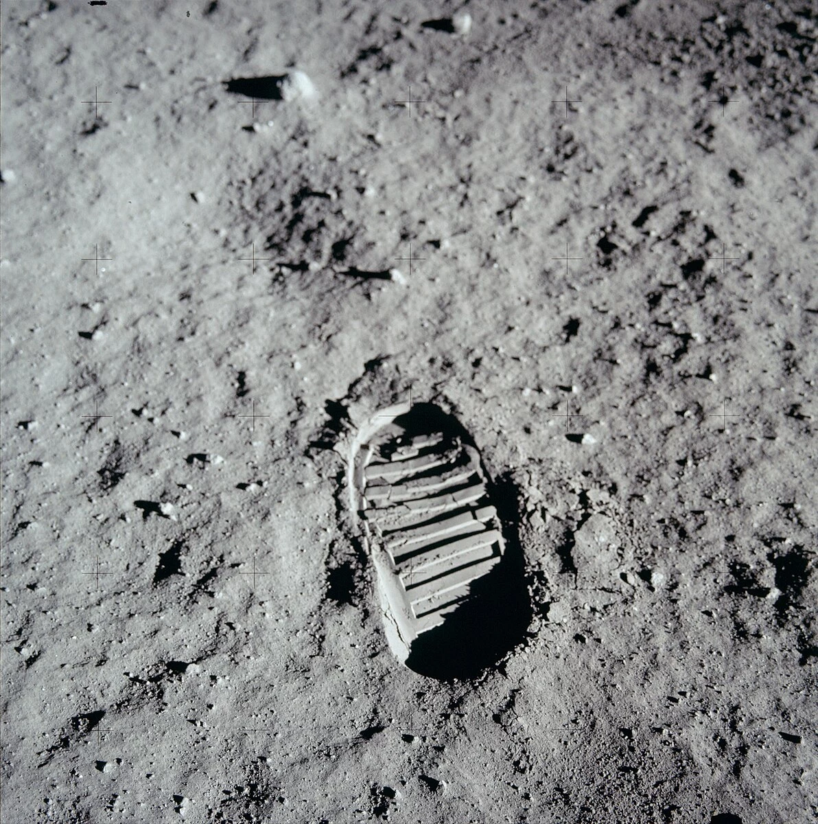 Odcisk buta astronauty w pyle księżycowym na powierzchni Księżyca, szczegółowo widoczne linie i struktura odcisku oraz drobne ziarenka pyłu wokół.