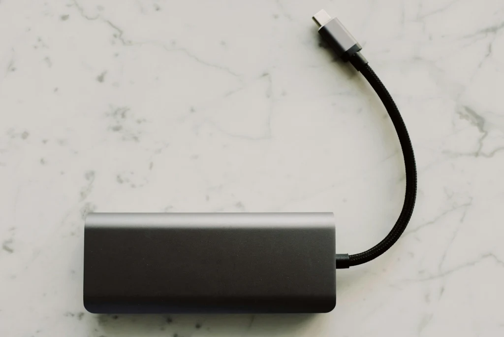 Jakie powerbanki są kompatybilne z samochodem? Szary adapter USB-C z krótkim kablem na jasnym, marmurowym blacie.