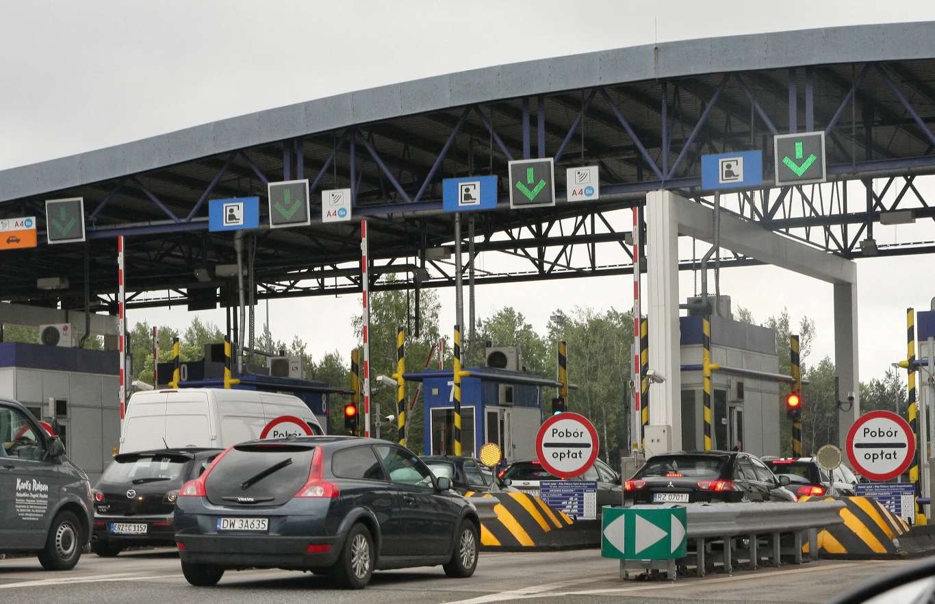 Nocne utrudnienia na A4. Zmiany w ruchu w rejonie Mysłowic. Samochody oczekujące w kolejce przed bramkami autostradowymi pod zadaszeniem, otoczenie oznakowane znakami drogowymi informującymi o konieczności pobrania opłaty, sygnalizacja świetlna reguluje ruch.