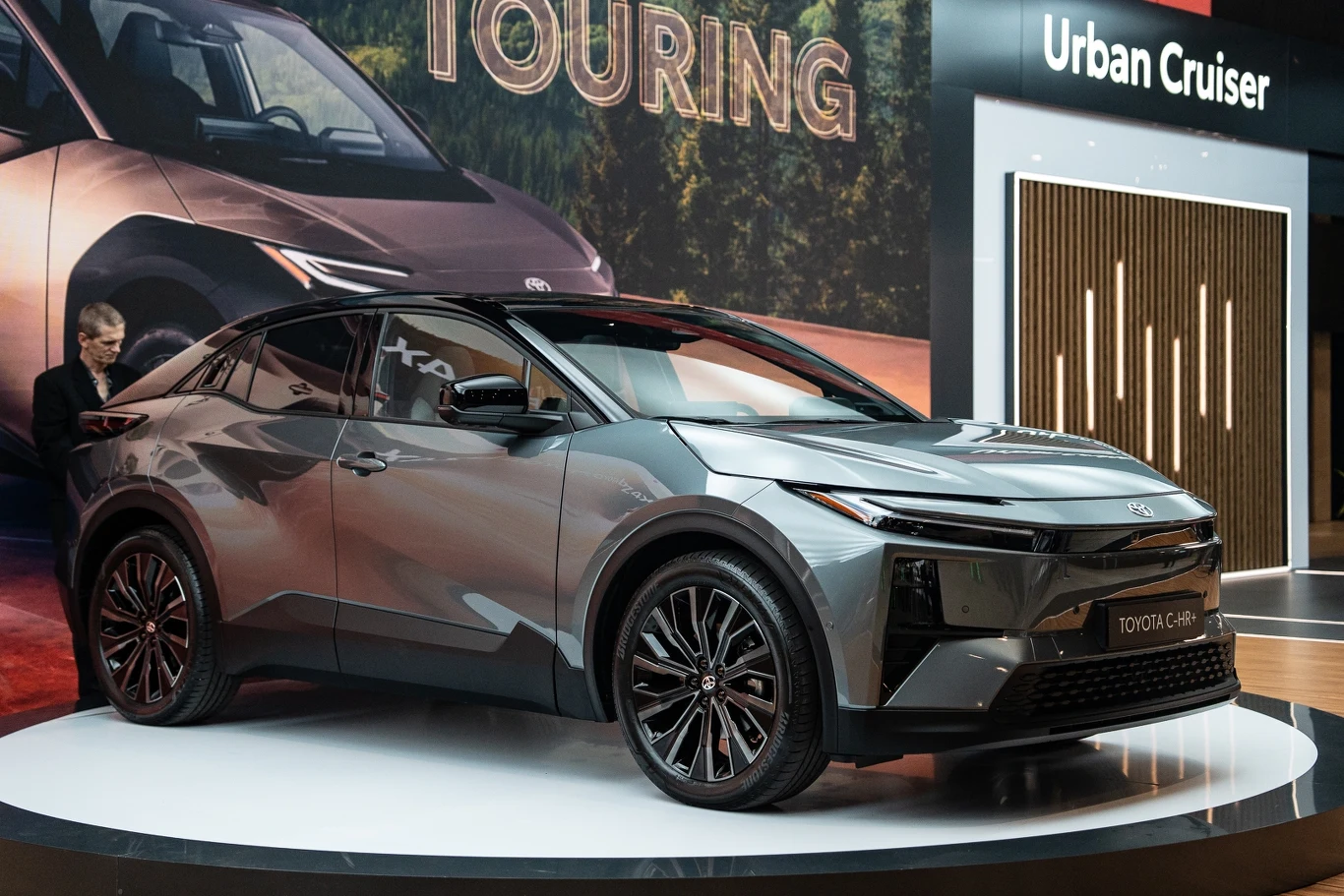 Na Kongresie Nowej Mobilności w Katowicach Toyota zaprezentowała aż cztery nowe samochody elektryczne dla Europy Nowoczesny, szary samochód osobowy Toyota C-HR stoi na podświetlonym podeście na tle ekspozycji motoryzacyjnej. Auto wyróżnia się ostrymi liniami nadwozia i dużymi, stylowymi felgami.