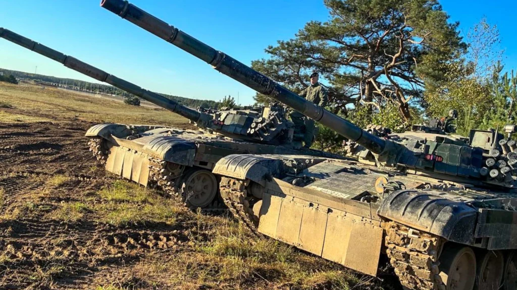 Dwa czołgi ustawione pod kątem na leśnym terenie, tło stanowi jasne niebo i drzewa, widoczne ślady po gąsienicach na ziemi