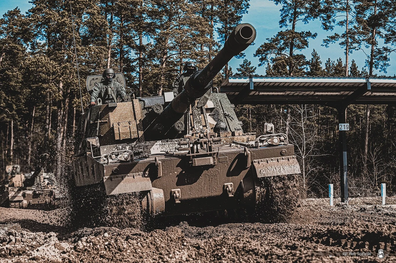 1 stycznia 2023 roku Agencja Uzbrojenia podpisała z Hanwha Defense drugą umowę wykonawczą na 152 armatohaubic K9, z których 148 ma być w spolonizowanej wersji K9PL Czołg poruszający się po błotnistym terenie, otoczony przez drzewa, z dwoma żołnierzami widocznymi na wieży; dynamiczna scena manewrów wojskowych.