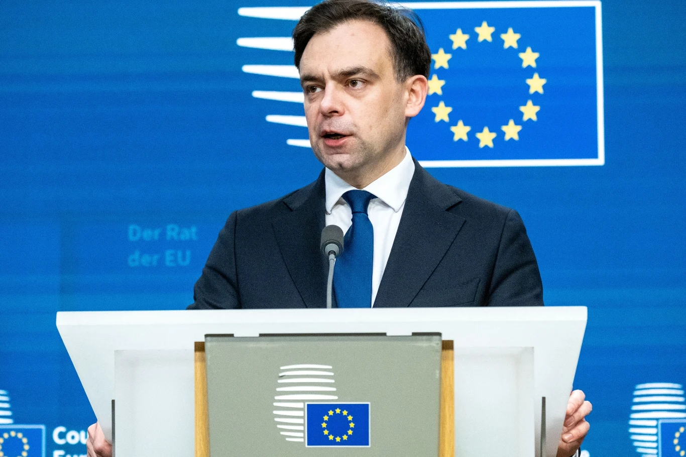Program pożyczek z KPO będzie miał negatywny wpływ na finanse publiczne w 2026 r. - pisze "Rzeczpospolita" Mężczyzna w garniturze stoi za mównicą z logo Unii Europejskiej, przemawiając podczas oficjalnego wydarzenia na tle niebieskiej ścianki z symbolem UE.