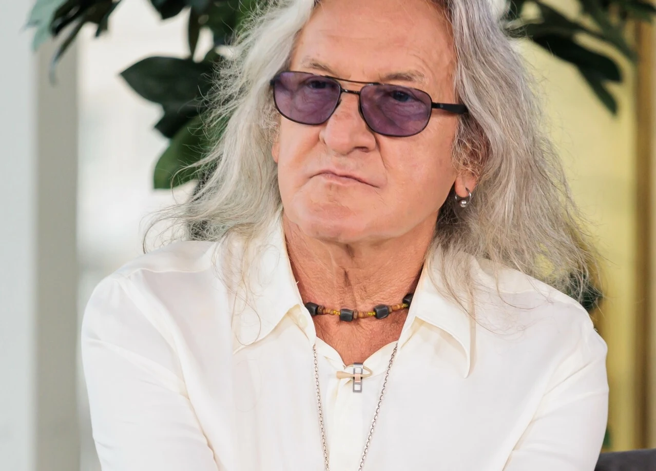 Grzegorz Markowski ma nieślubnego syna Mężczyzna z długimi siwymi włosami, ubrany w białą koszulę, z naszyjnikiem na szyi oraz okularami przeciwsłonecznymi o fioletowych szkłach, siedzi na tle zieleni.