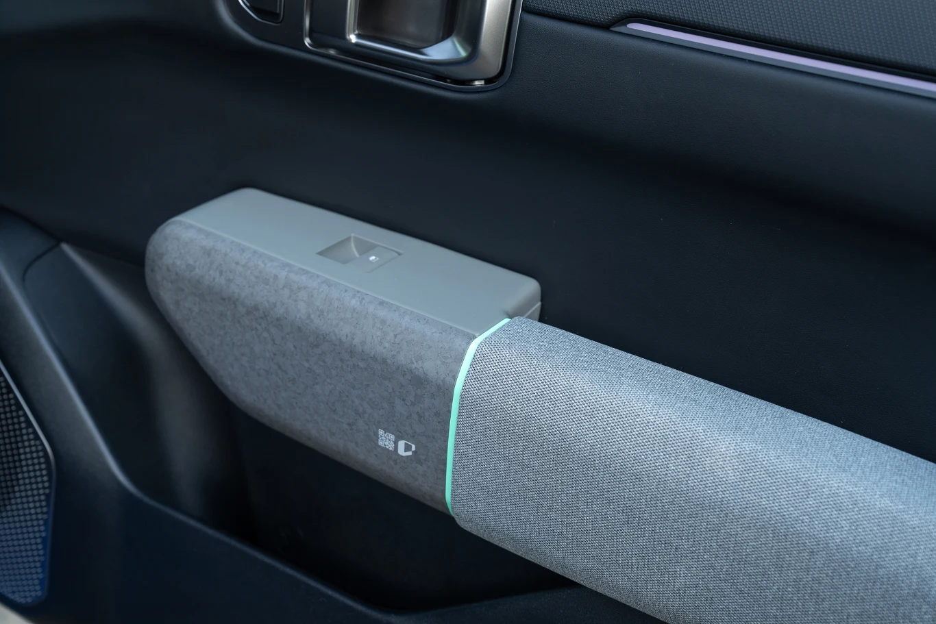 Jeden z rzadko spotykanych elementów, czyli plastikowe wstawki udające kamień. Element tapicerki drzwi samochodu, obejmujący podłokietnik z tkaniny o wyrazistej fakturze oraz prostokątny panel z plastikowym wykończeniem i ikoną otwierania szyb.