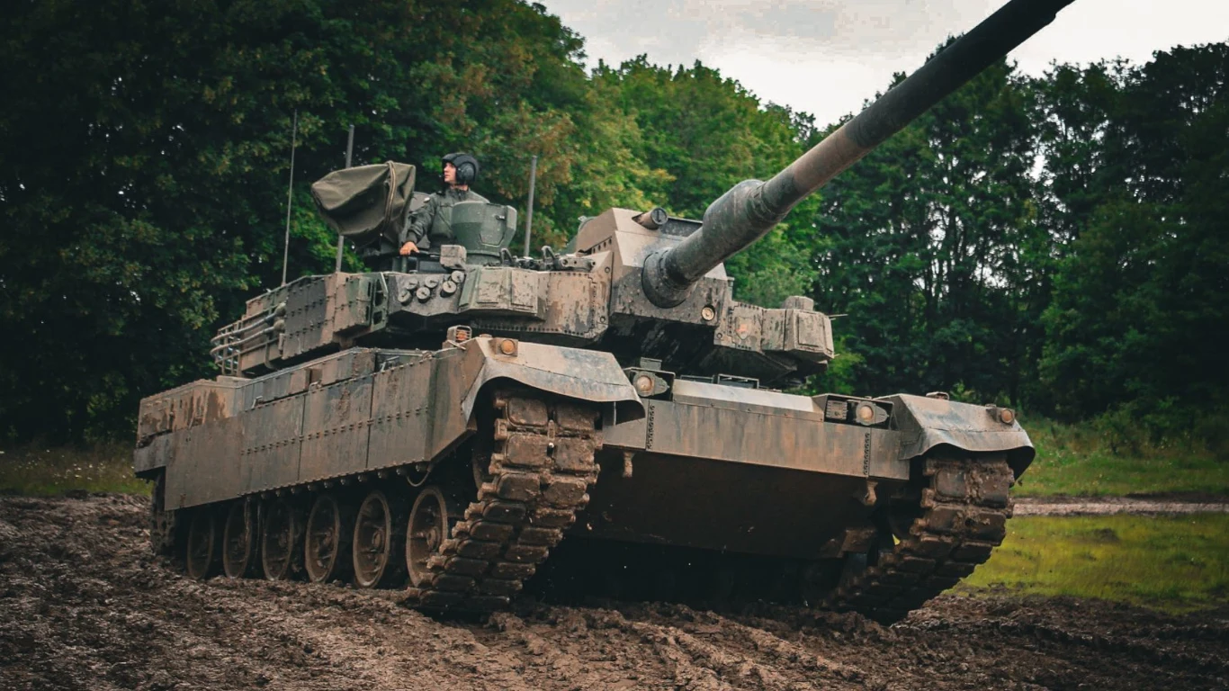 Czołgi w nowej konfiguracji K2PL zostaną wyposażone w system ASOP, system antydronowy oraz dodatkowe opancerzenie Nowoczesny czołg gąsienicowy poruszający się po błotnistym terenie, z żołnierzem widocznym w wieżyczce i gęstym, zielonym lasem w tle.