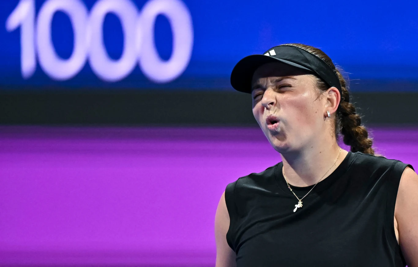Jelena Ostapenko Tenisistka w czarnej koszulce i czapce z daszkiem, z wyrazem emocji na twarzy, na tle fioletowego kortu z dużym napisem 1000 w tle.