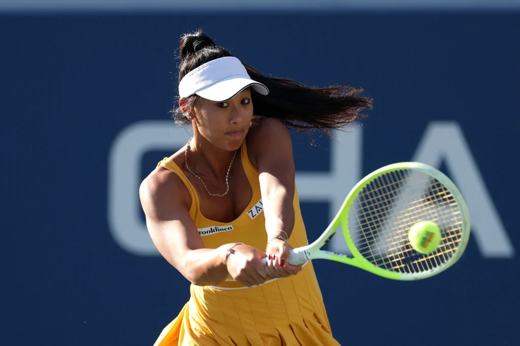 Priscilla Hon Kobieta w żółtej sukience sportowej i białej czapce odbijająca piłkę tenisową podczas meczu, z widoczną koncentracją w trakcie uderzenia rakietą.