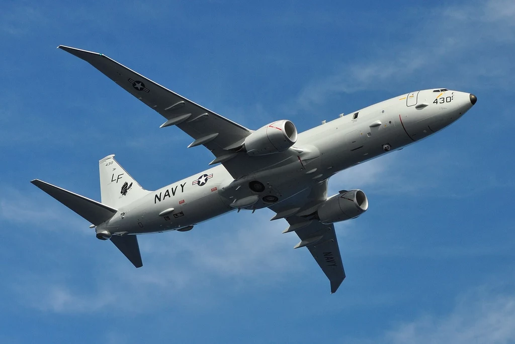 Wojskowy samolot patrolowy US Navy Boeing P-8 Poseidon w locie na tle niebieskiego nieba, wyraźnie widoczne oznaczenia i detale konstrukcyjne maszyny.
