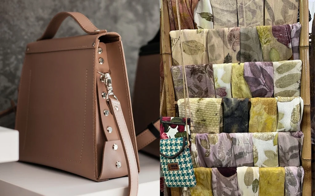 Dodatki to kwintesencja francuskich stylizacji Beżowa torebka z metalowymi nitami stojąca na jasnej półce, obok stojak z tkaninami o wzorach liści w odcieniach zieleni, żółci, fioletu i beżu.