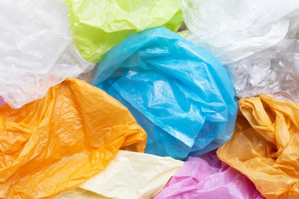 Kolorowe, pogniecione plastikowe torby ułożone warstwowo, wśród których dominują odcienie niebieskiego, pomarańczowego, żółtego, zielonego, bieli i różu.
