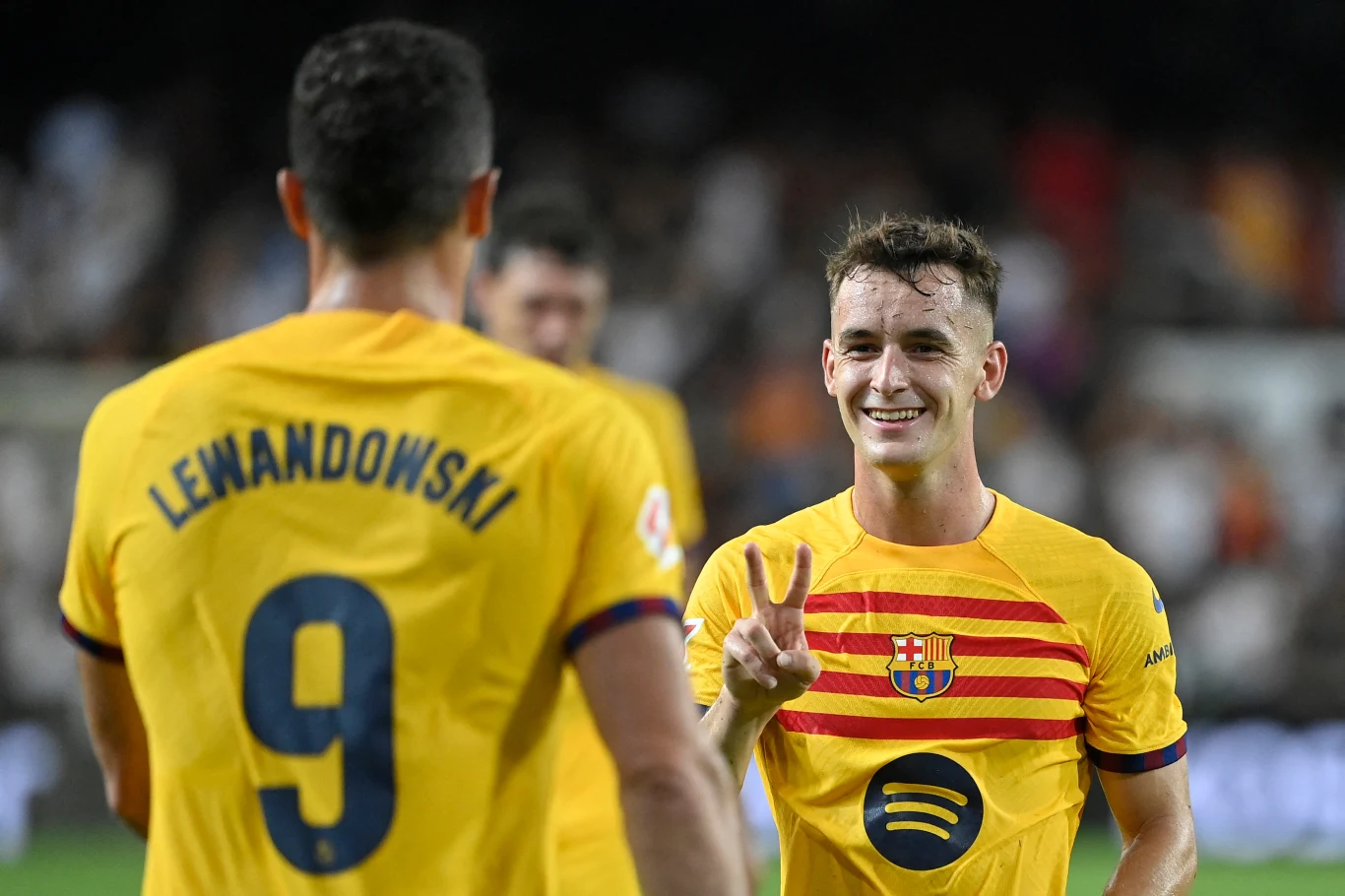 Dwóch piłkarzy FC Barcelony w żółtych koszulkach drużyny na boisku, jeden z nich pokazuje znak pokoju dłońmi, obaj wyglądają na zadowolonych po zakończonym meczu