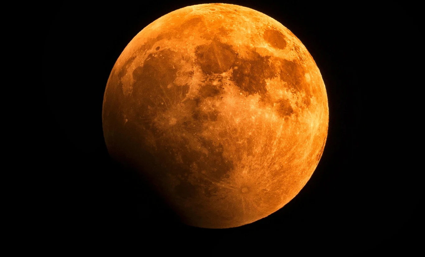 Księżyc rdzewieje, to nie żart! Powierzchnia Księżyca częściowo pokryta cieniem, widoczna efektowna czerwona barwa oraz detale kraterów i struktur, tło całkowicie czarne podkreślające obiekt na pierwszym planie.