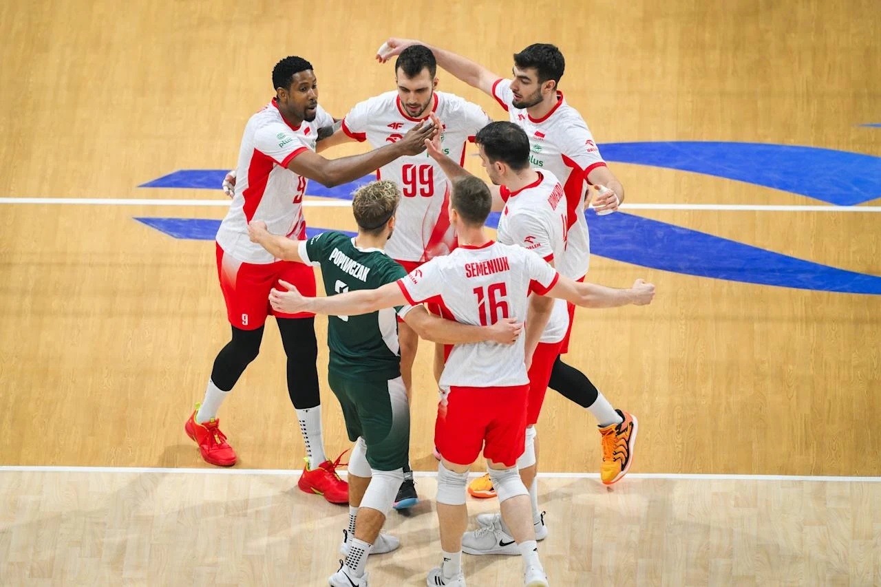 Siatkarze reprezentacji Polski podczas meczu o brązowy medal Grupa siatkarzy ubranych w białe i czerwone stroje świętuje zdobycie punktu na środku boiska, zawodnicy obejmują się i okazują radość, tło stanowi drewniana podłoga hali sportowej.