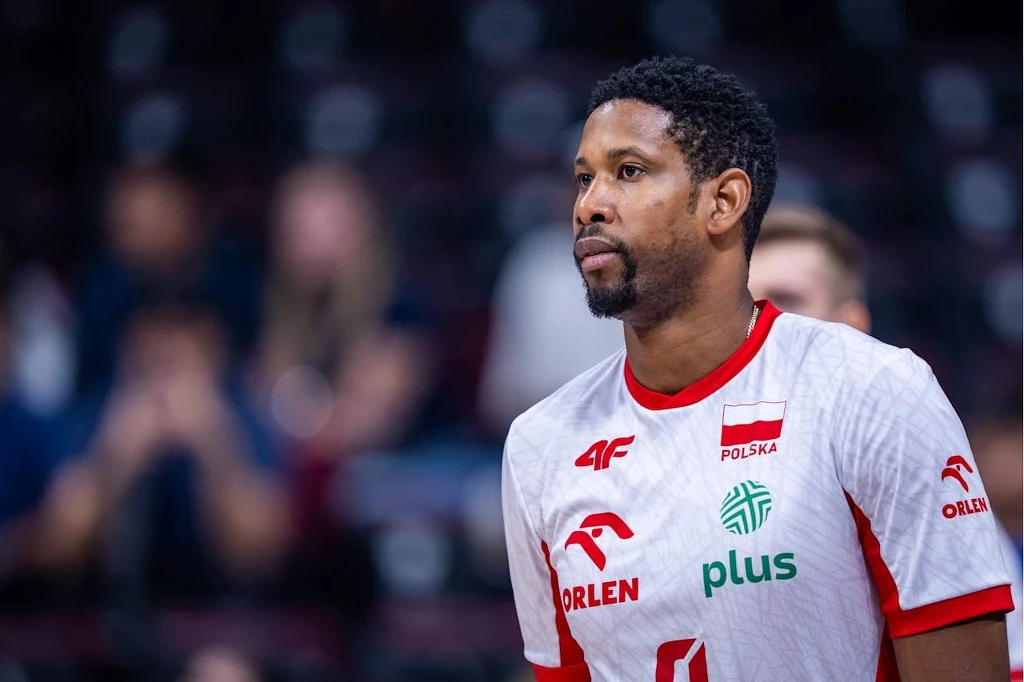 Siatkarz w polskim stroju reprezentacyjnym z logotypami sponsorów, koncentrujący się podczas meczu, w tle rozmyta publiczność.