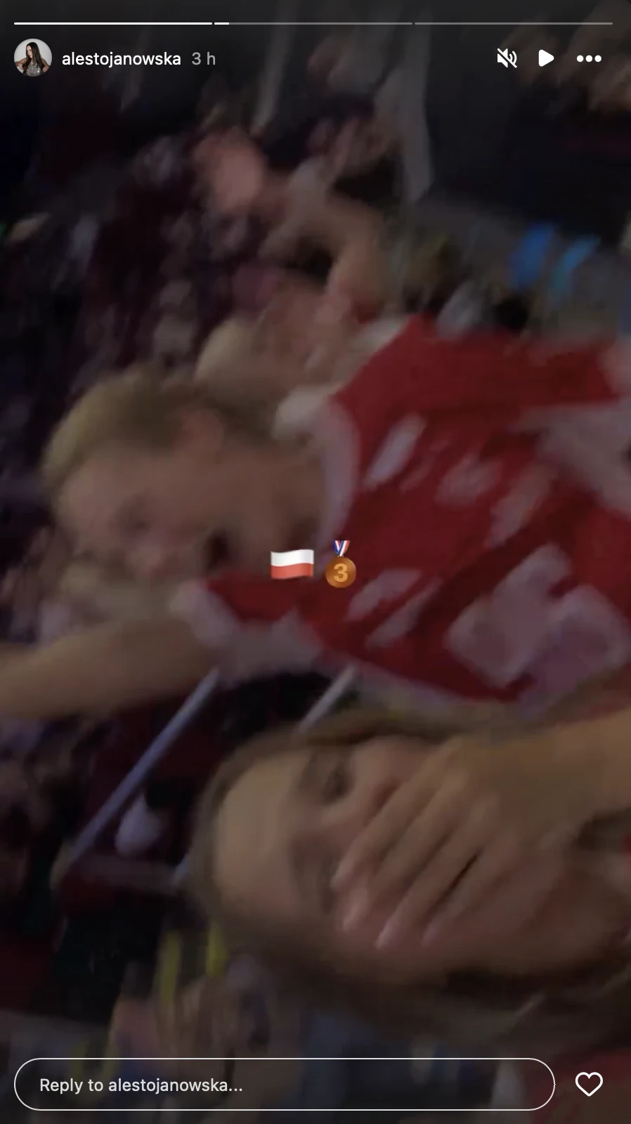 Dwie osoby w tłumie kibiców, jedna z nich w czerwonej koszulce sportowej unosi rękę w geście radości, druga zakrywa twarz dłonią i uśmiecha się, w tle widoczne rozmyte sylwetki innych kibiców.