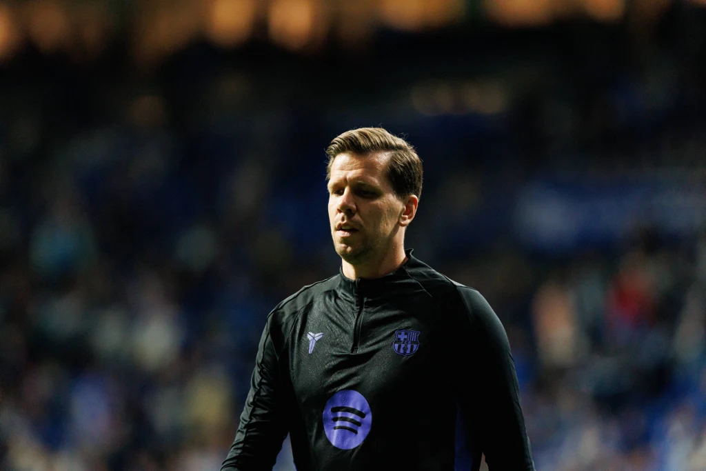 Wojciech Szczęsny Mężczyzna w sportowym stroju, z logo Spotify na bluzie, stoi na tle rozmytego stadionu, światło pada na jego twarz, nadając scenie poważny nastrój.