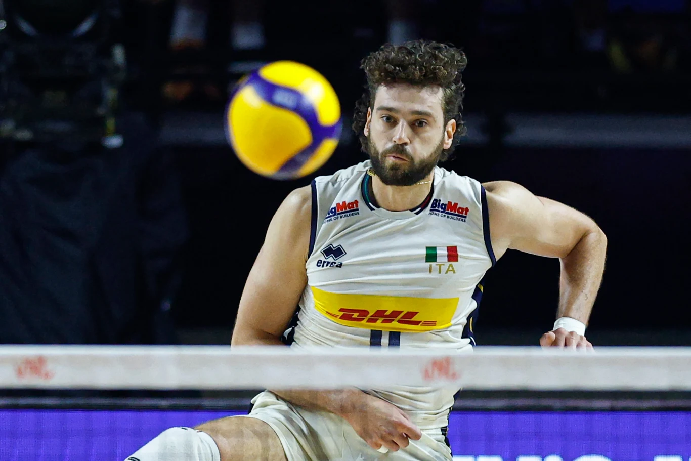 Kamil Rychlicki Siatkarz włoskiej reprezentacji w białym stroju z logo sponsora koncentruje się na lecącą nad siatką piłkę podczas meczu siatkówki.