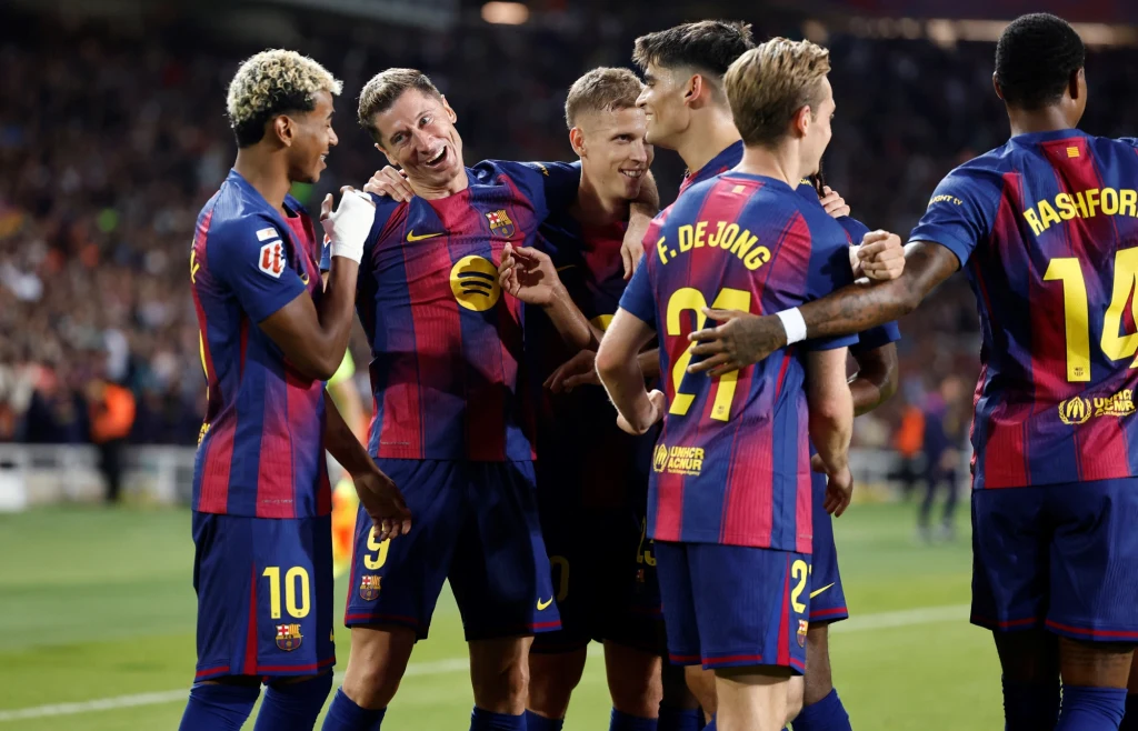 Piłkarze Barcelony Grupa piłkarzy w granatowo-bordowych strojach świętuje na murawie stadionu, otoczona tłumem kibiców, w tle rozmyty stadion wypełniony widzami.