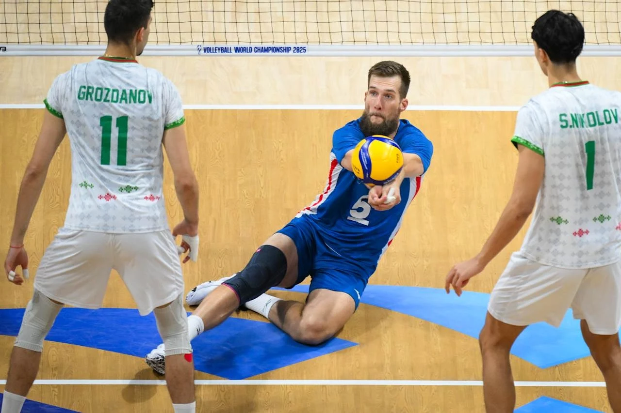 Adam Zajicek po MŚ kończy z grą w reprezentacji Czech Siatkarz w niebieskim stroju wykonuje efektowną obronę wślizgiem przy parkiecie, podczas gdy dwóch zawodników drużyny przeciwnej w białych strojach obserwuje akcję.