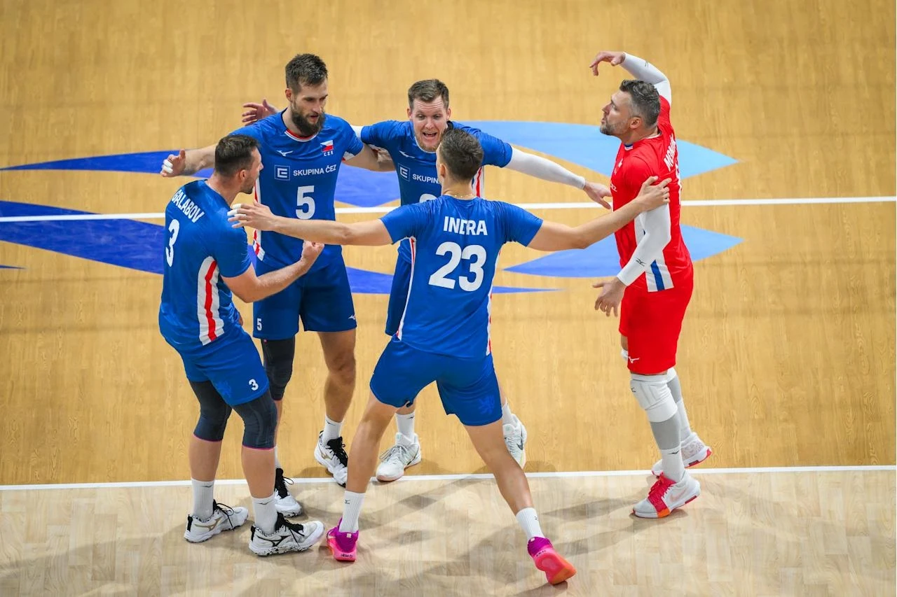 Siatkarze z Czech, drugi z lewej Adam Zajicek Grupa siatkarzy w niebieskich i czerwonym stroju świętuje zdobycie punktu na boisku, zawodnicy stoją w okręgu z wyciągniętymi rękami, radość i sportowa atmosfera są dominujące w scenie.