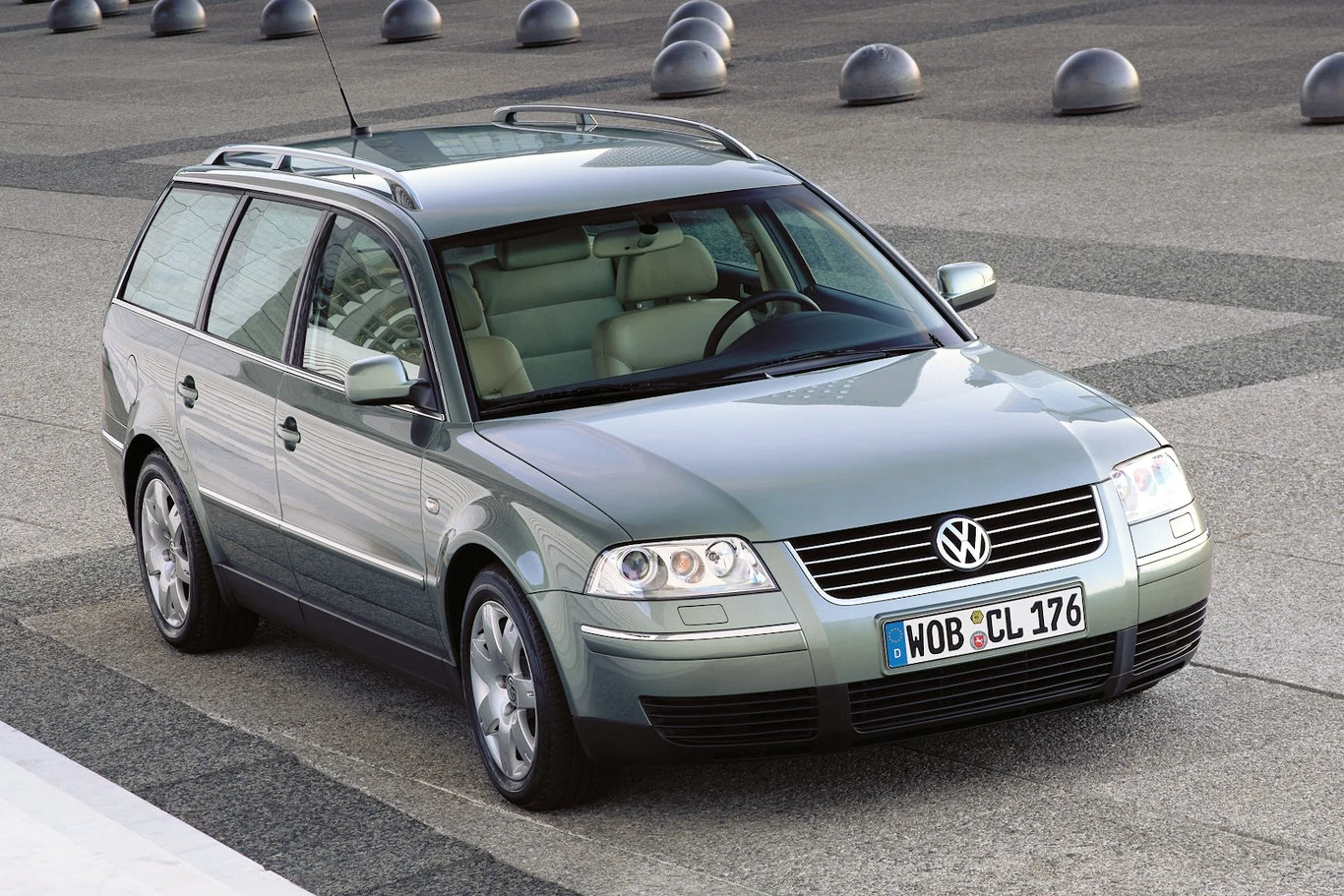 Srebrny samochód osobowy typu kombi marki Volkswagen Passat zaparkowany na nowoczesnym, miejskim placu o betonowej nawierzchni, w tle charakterystyczne kule architektoniczne.