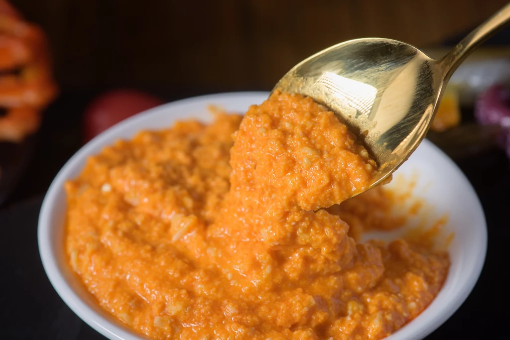 Gęsta pomarańczowa pasta lub dip w białej miseczce, mieszana złotą łyżką.