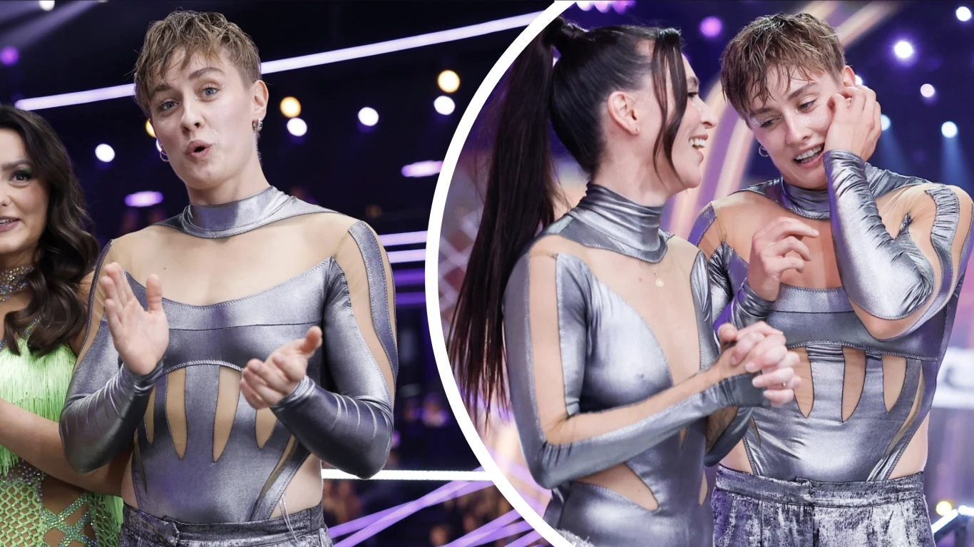 Katarzyna Zillmann w "Tańcu z Gwiazdami" Dwie osoby w srebrnych, połyskujących kostiumach scenicznych rozmawiają i śmieją się podczas programu rozrywkowego, w tle inne osoby oraz scenografia z jasnym oświetleniem.