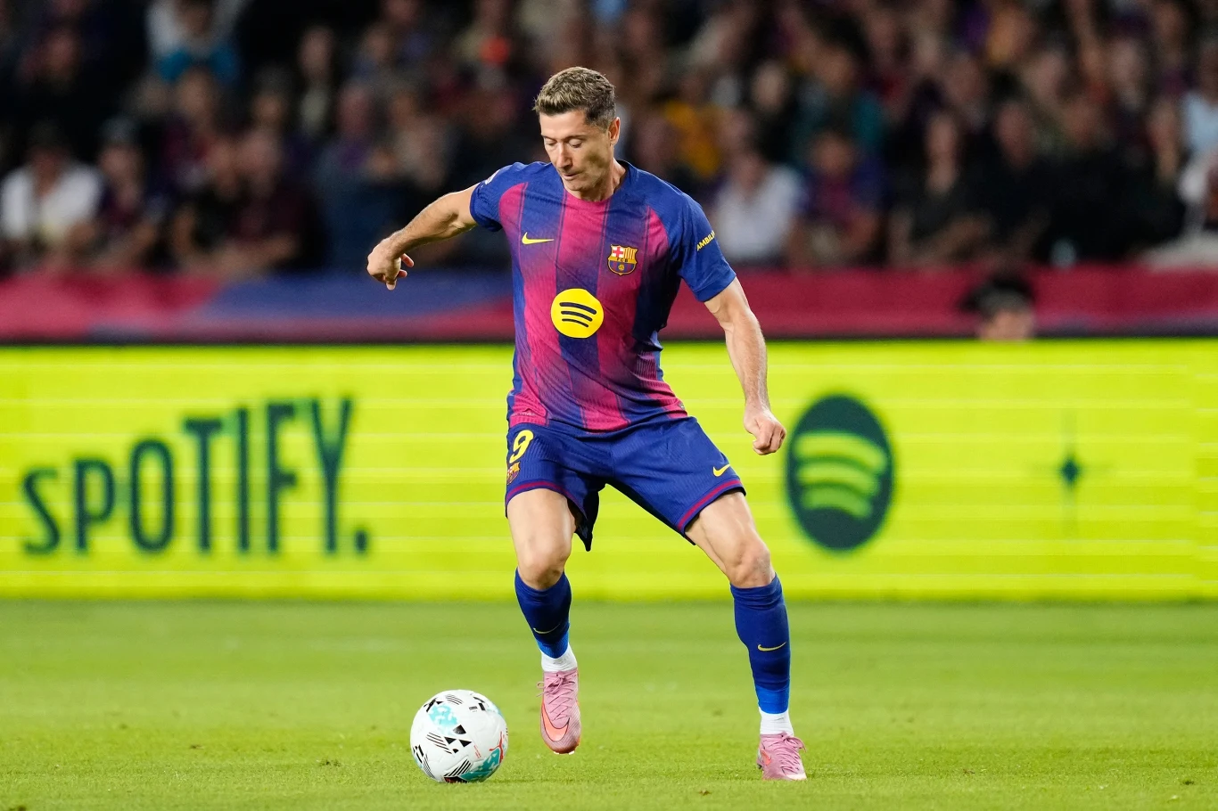 Piłkarz FC Barcelony w trakcie prowadzenia piłki na stadionie, na tle reklamy Spotify, w otoczeniu publiczności.