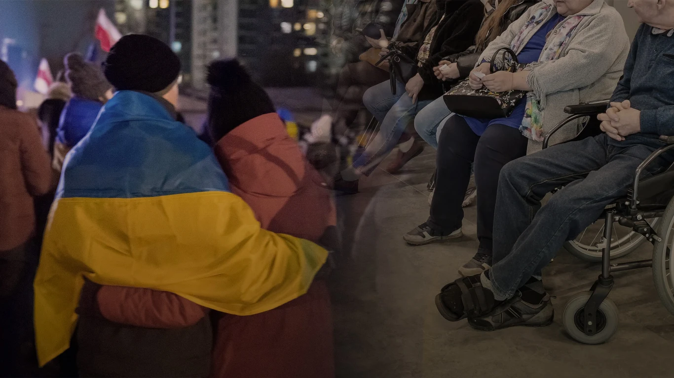 30 września wchodzą w życie zmiany dla Ukraińców w Polsce Osoba okryta ukraińską flagą obejmuje drugą osobę w tłumie podczas wydarzenia publicznego, w tle widoczne osoby siedzące na wózkach inwalidzkich oraz ludzie na widowni.