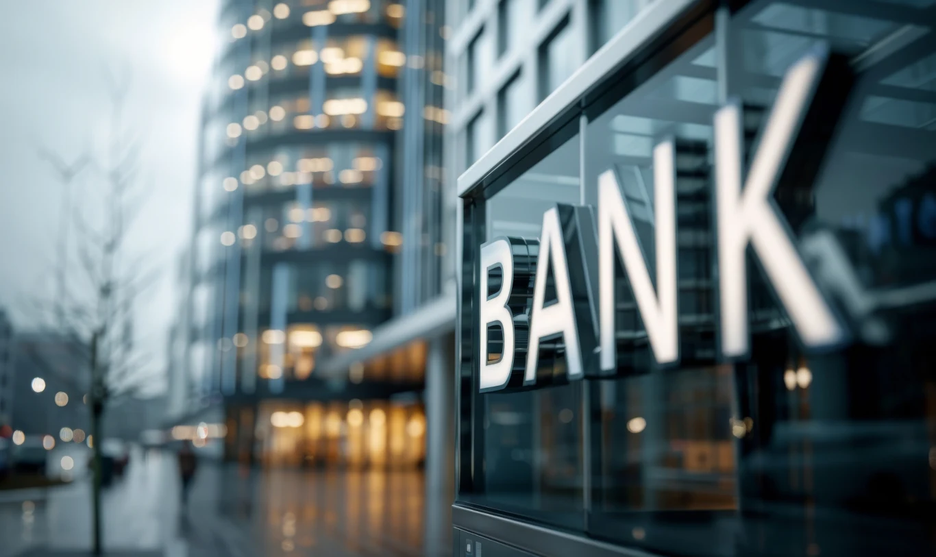 Ustawa frankowa ma wspierać konsumentów w sporach z bankami. Zdj. ilustracyjne Nowoczesny budynek banku z dużym, podświetlonym napisem, w tle szklane fasady wysokich biurowców i rozmyte światła miasta wieczorem.